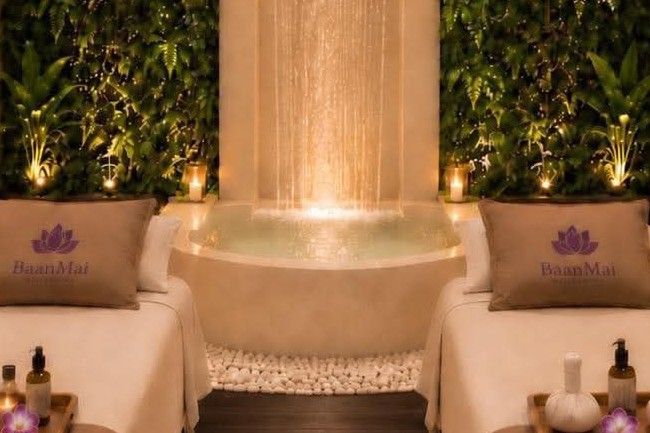 A lit water curtain falling into a stone bath ringed by white pebbles and candles.